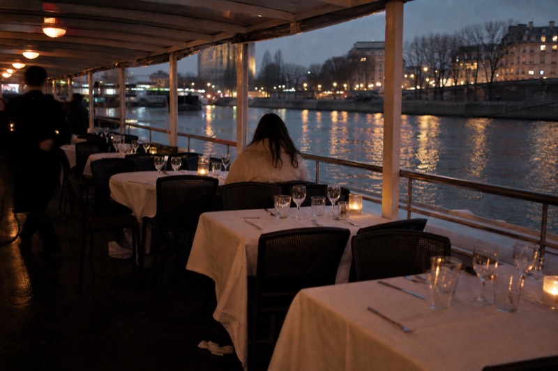 Dinner tables set on the covered deck of a Savannah riverboat at dusk, city lights reflecting on the Savannah River
