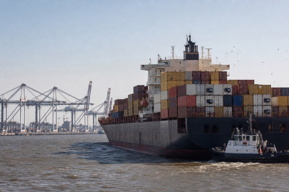 Large cargo ship and tugboat moving on the Savannah River with the city behind, no text, no logos, no people