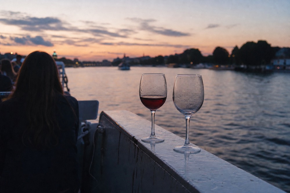 Two glasses resting on a boat rail above the river at dusk, no text, no logos, no people