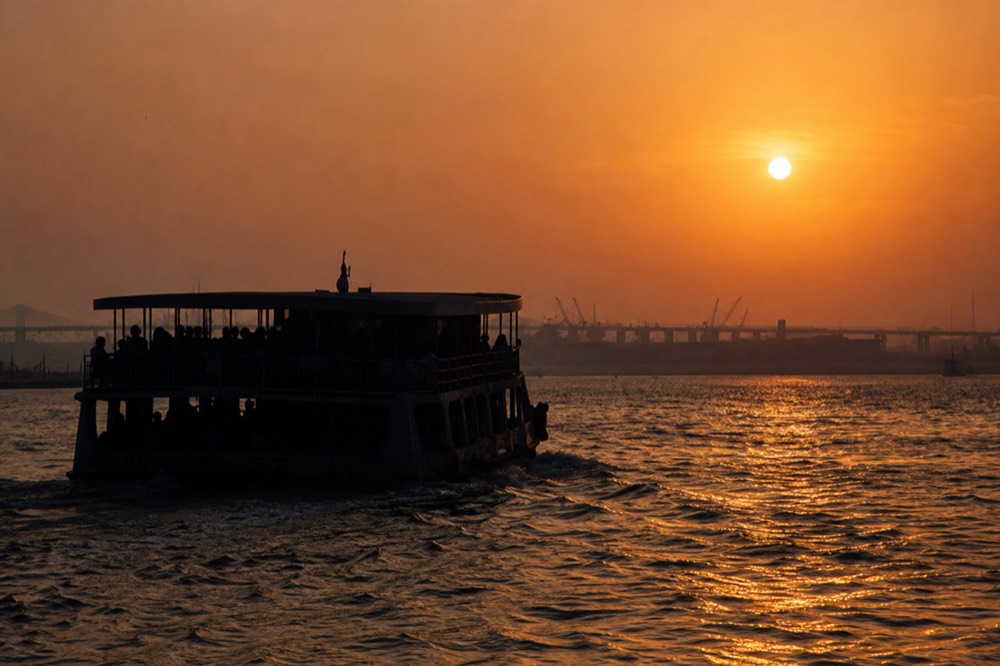A riverboat silhouette against an orange sunset sky over the water, no text, no logos, no people