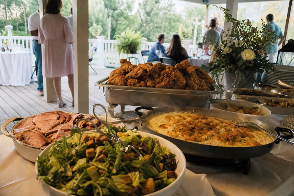 A Southern brunch buffet spread with fried chicken, shrimp and grits and salads on a riverboat deck, no text, no logos, no people