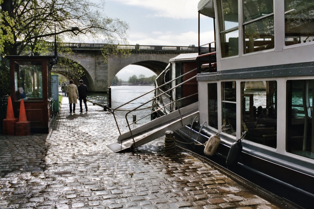 A ticket booth and dock on East River Street with a paddlewheel riverboat waiting to board, no text, no logos, no people