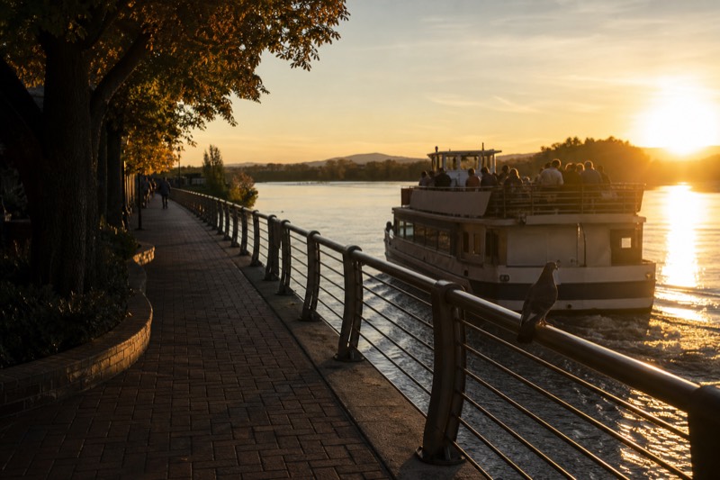 Passengers along the rail of a Savannah riverboat as the sky turns orange over the river at sunset, departing from the historic River Street waterfront in downtown Savannah
